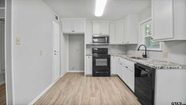 a kitchen with a hard wood floor white cabinets and stainless steel appliances