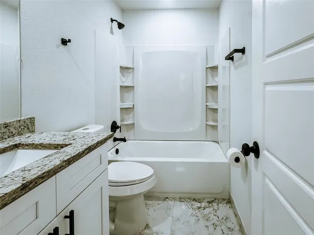 a bathroom with a granite countertop bathtub shower sink vanity and toilet
