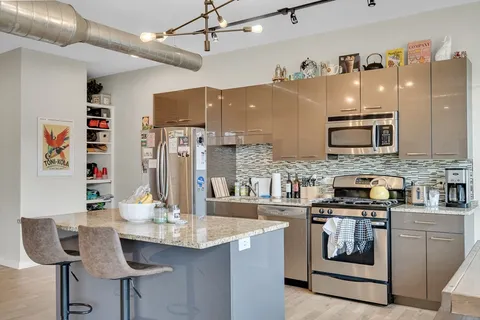 a kitchen with stainless steel appliances kitchen island granite countertop a table chairs in it and wooden floors