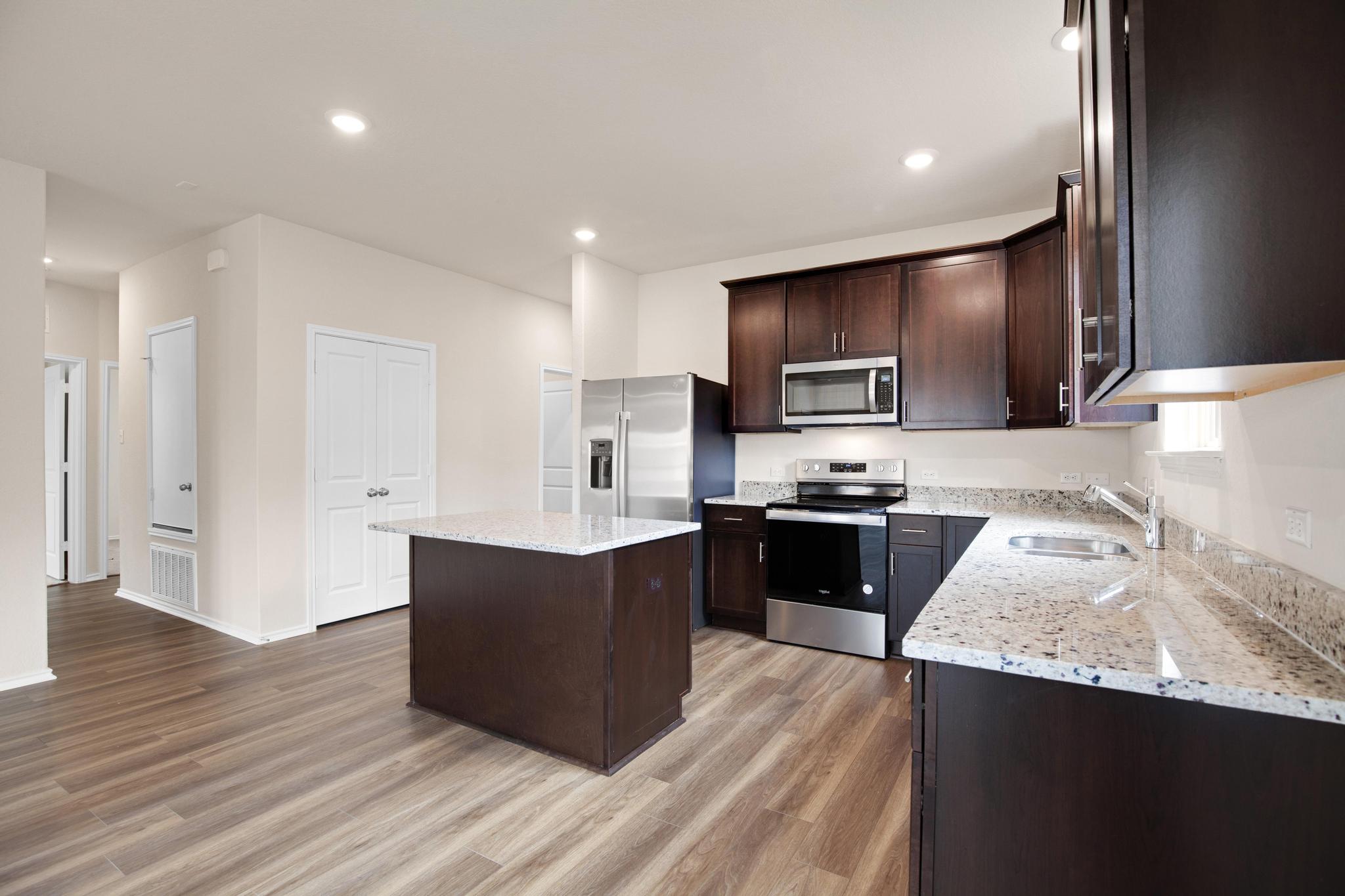 200 Janice Road Taylor, TX 76574 - Photo 5 of 25 A well-lit kitchen features rich cabinetry, stone counters, and a central island, perfect for culinary endeavors.