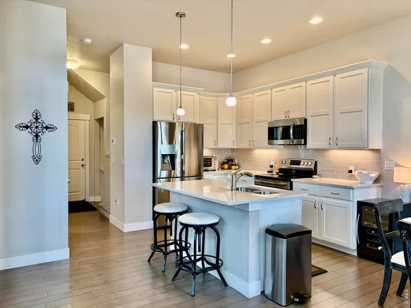 a kitchen with stainless steel appliances kitchen island granite countertop a refrigerator a stove a sink a dining table and chairs with wooden floor