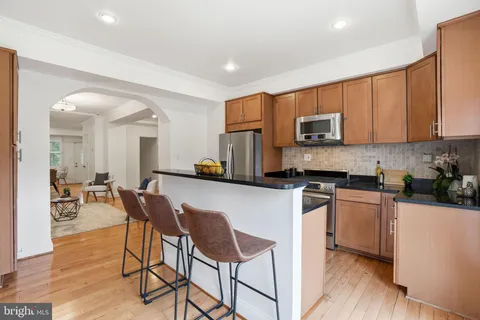 a kitchen with stainless steel appliances kitchen island granite countertop a stove a sink a refrigerator a dining table and chairs with wooden floor