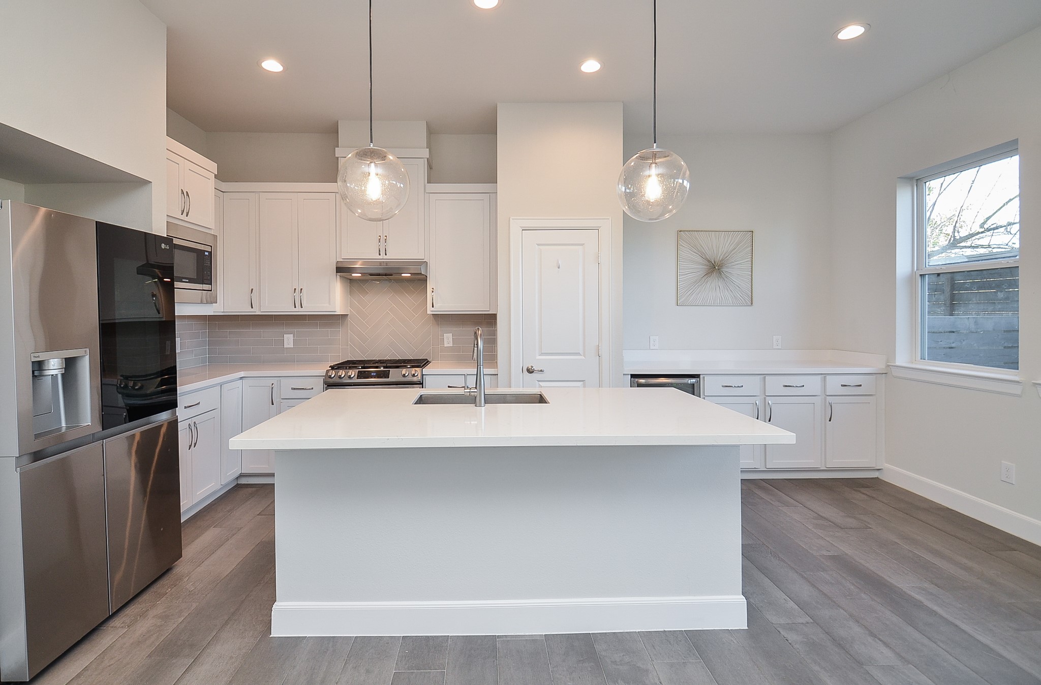 9577 Neuens Road, Unit F Houston, TX 77080 - Photo 3 of 26 Contemporary kitchen with quartz countertops, stainless steel appliances, ample cabinetry, and breakfast bar seating—stylishly finished with continuous wood-look tile flooring.