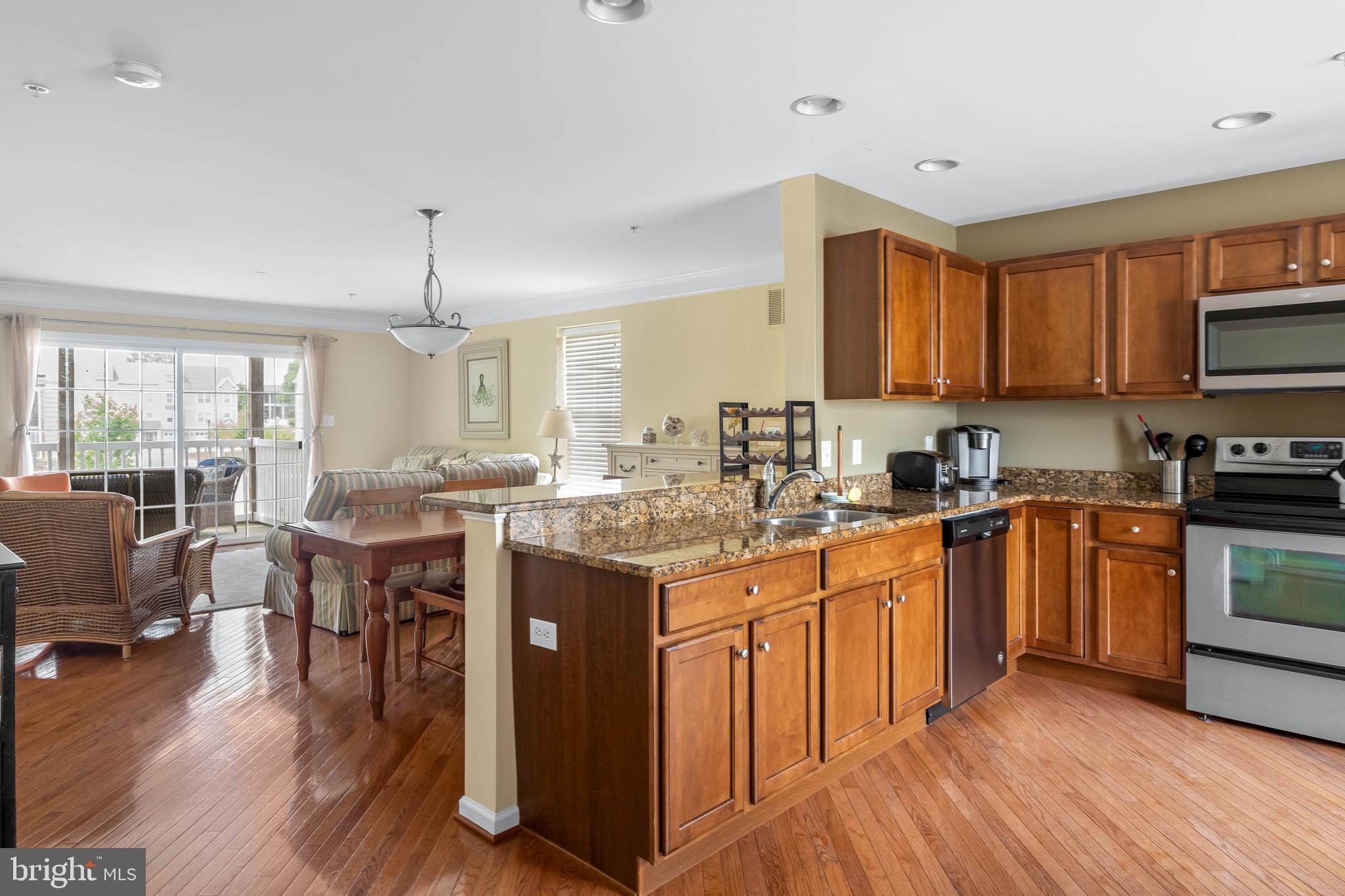 19901 Ames Drive, Unit 133 Rehoboth Beach, DE 19971 - Photo 6 of 34 a kitchen with stainless steel appliances granite countertop a stove top oven a sink a dining table and chairs with wooden floor