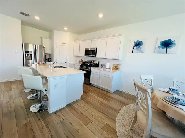 a large white kitchen with a stove a sink dishwasher and a refrigerator with wooden floor