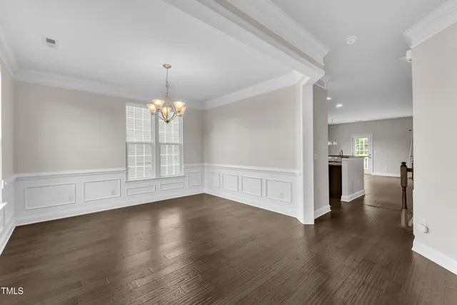 a view of empty room with wooden floor and kitchen