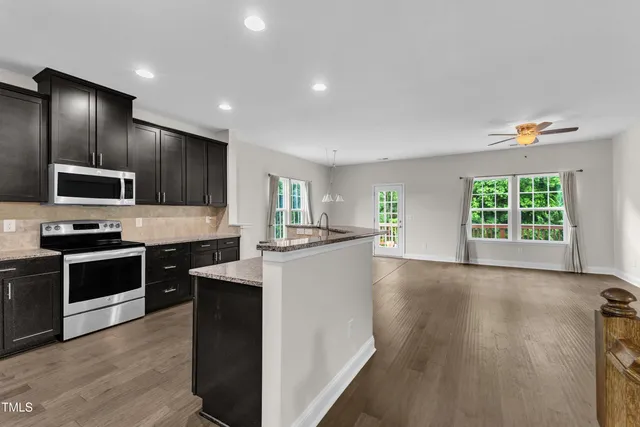 a large kitchen with stainless steel appliances granite countertop a stove a sink dishwasher a microwave oven and a refrigerator with wooden floor