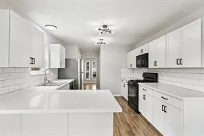 a very nice looking kitchen with granite countertop a sink dishwasher stove and white cabinets with wooden floor