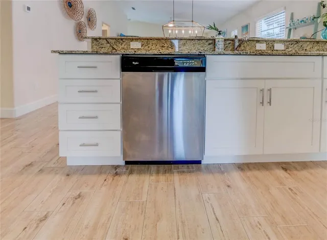 a kitchen with stainless steel appliances granite countertop a refrigerator a stove a sink dishwasher and white cabinets with wooden floor