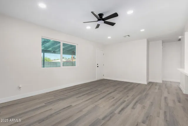an empty room with wooden floor ceiling fan and windows