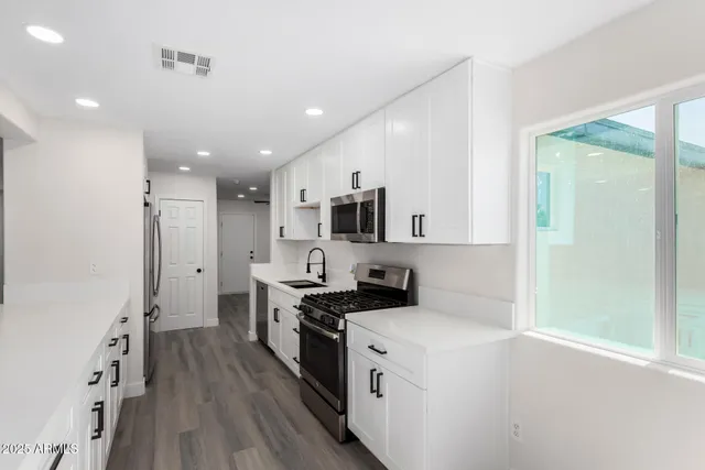 a kitchen with stainless steel appliances a stove top oven a sink a refrigerator white cabinets and wooden floor