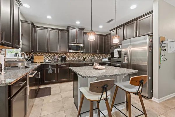 a kitchen with stainless steel appliances kitchen island granite countertop a refrigerator a stove a kitchen island a dining table and chairs