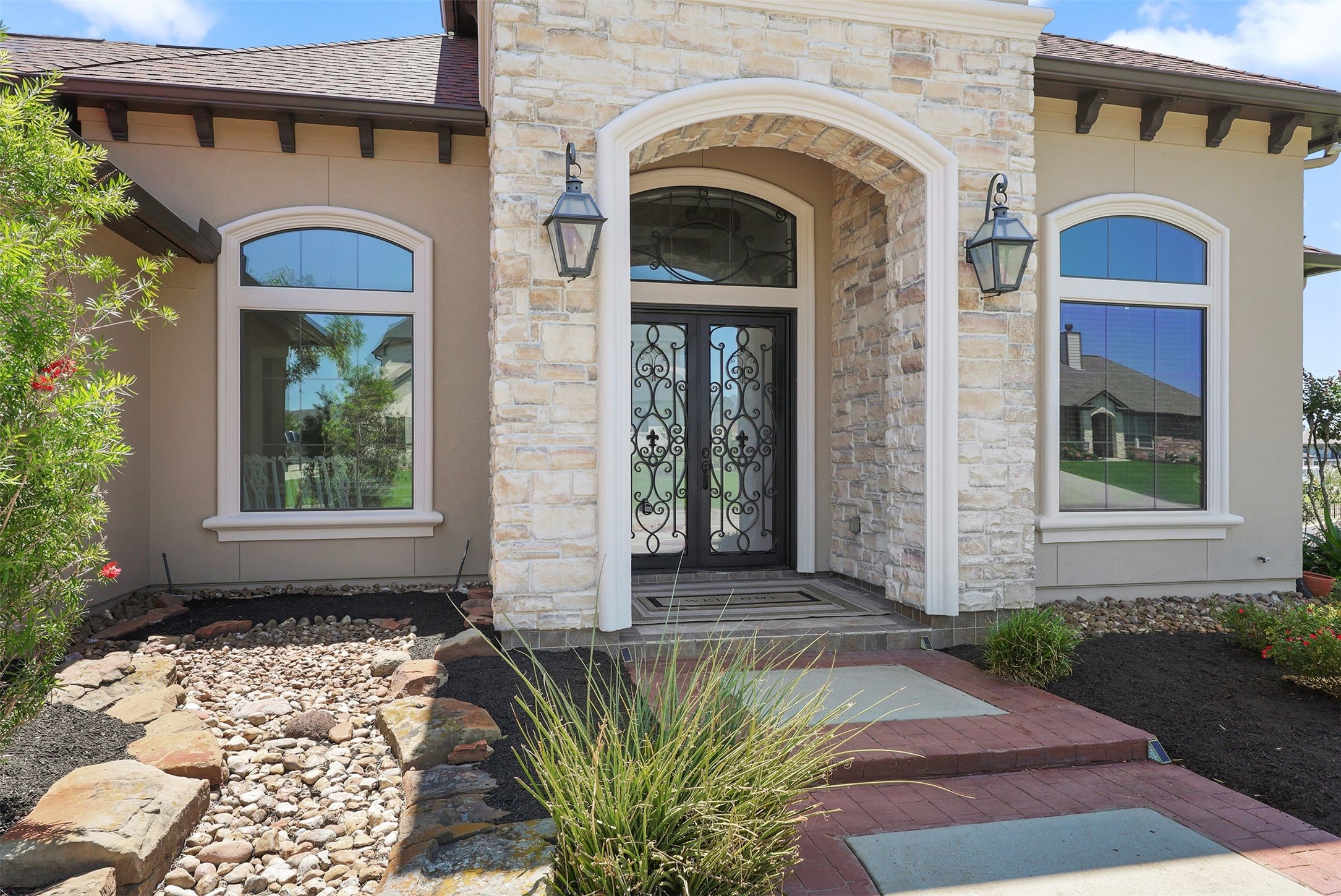 10896 Decatur Street Willis, TX 77318 - Photo 11 of 50 This elegant home boasts a stunning stone facade with large arched windows and a decorative wrought iron front door, complemented by a stone walkway and meticulously maintained landscaping that enhances its welcoming curb appeal.