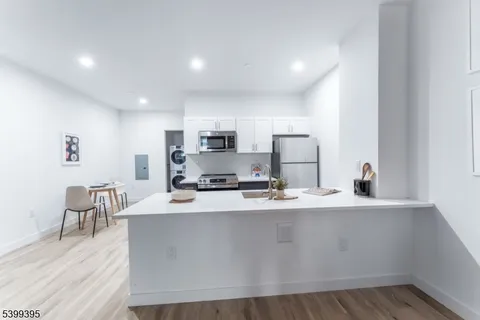 a kitchen with stainless steel appliances a sink a stove a refrigerator with white cabinets and wooden floor