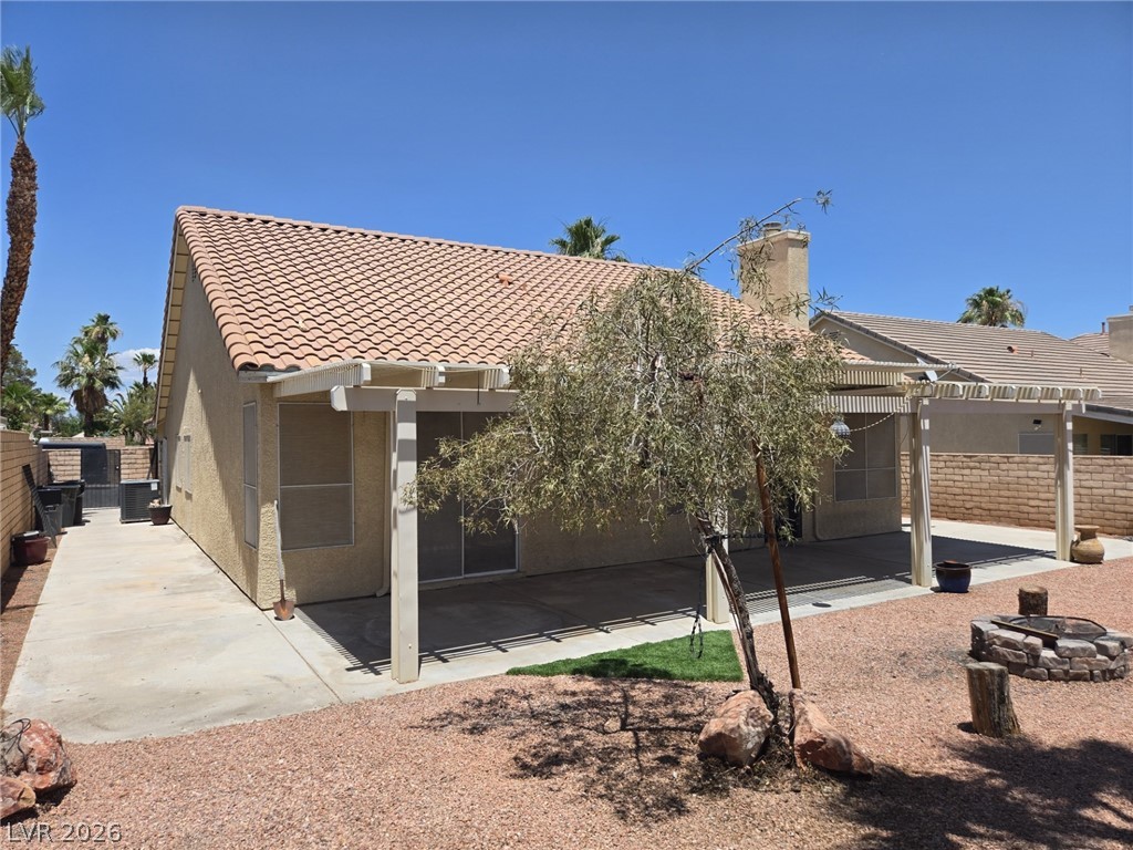 8417 San Ramon Drive Las Vegas, NV 89147 - Photo 31 of 33 An inviting backyard patio features a pergola, mature tree, and a stone fire pit, perfect for outdoor relaxation.