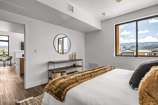 a bedroom with a bed a mirror and a large window with wooden floor