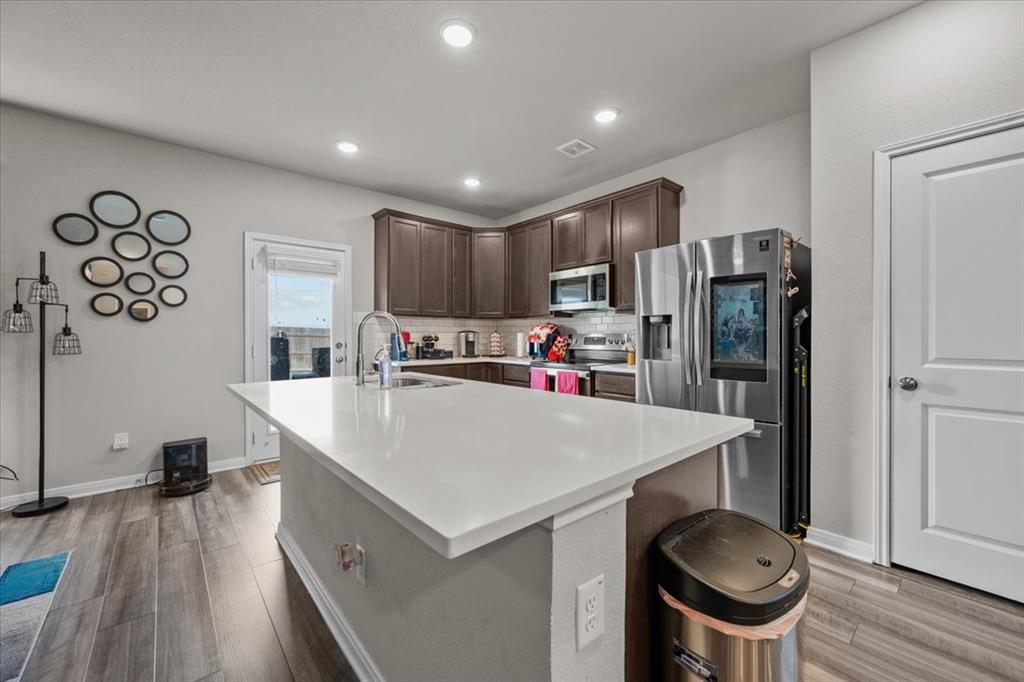 3501 Beutel Road Lorena, TX 76655 - Photo 8 of 33 Kitchen with appliances with stainless steel finishes, decorative backsplash, light countertops, dark brown cabinets, and light wood finished floors