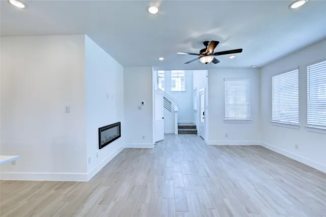 an empty room with wooden floor ceiling fan and windows