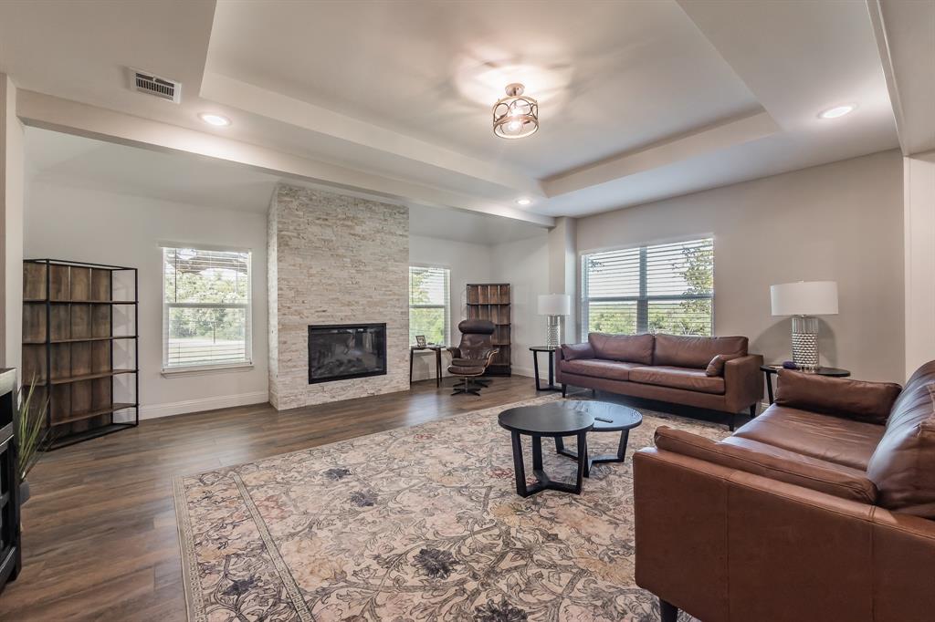 117 Rock Salt Drive Springtown, TX 76082 - Photo 9 of 38 Spacious living area featuring wood-finish flooring, a stacked stone fireplace with a black insert, and a tray ceiling with recessed lighting