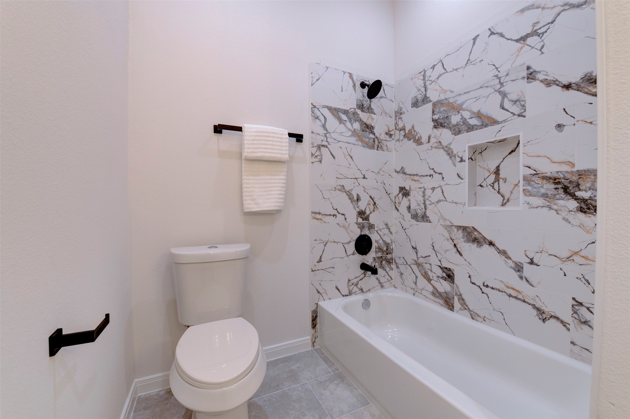 6807 Paris Street Houston, TX 77021 - Photo 38 of 50 Tub/shower combo with dramatic marble-look tile surround, built-in niche, matte black shower fixtures, and tile flooring.