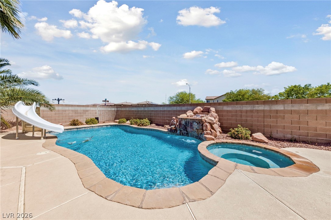 An inviting backyard oasis awaits with a sparkling pool, slide, and rock waterfall feature.