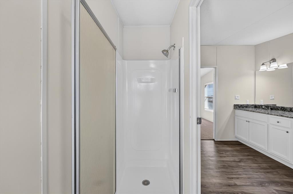 246 PR-4443 Rhome, TX 76078 - Photo 15 of 35 Shower with a sliding glass enclosure, a white vanity with dual sinks, a dark countertop, and wood-finish flooring