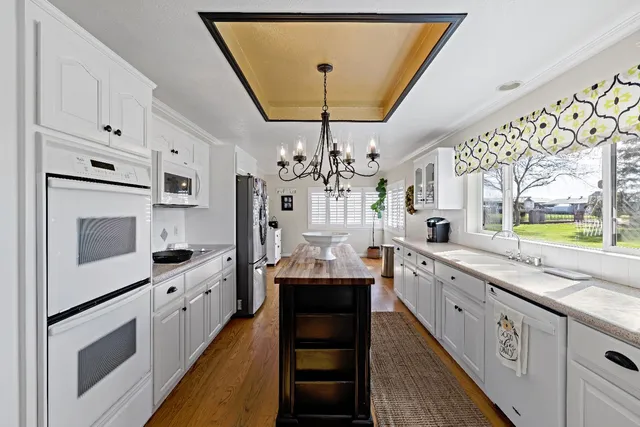 a large white kitchen with stainless steel appliances granite countertop a stove a sink dishwasher and white cabinets with wooden floor