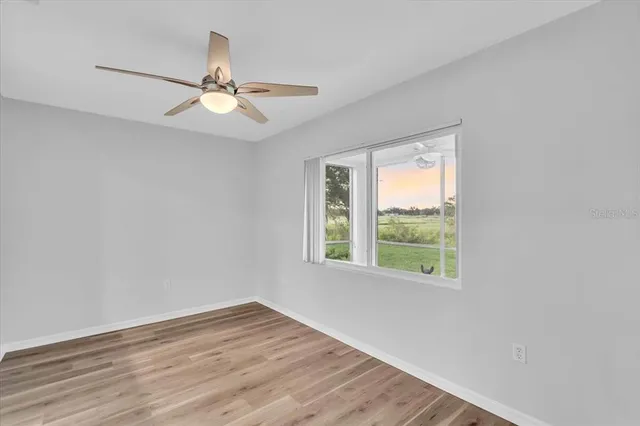 an empty room with wooden floor fan and windows