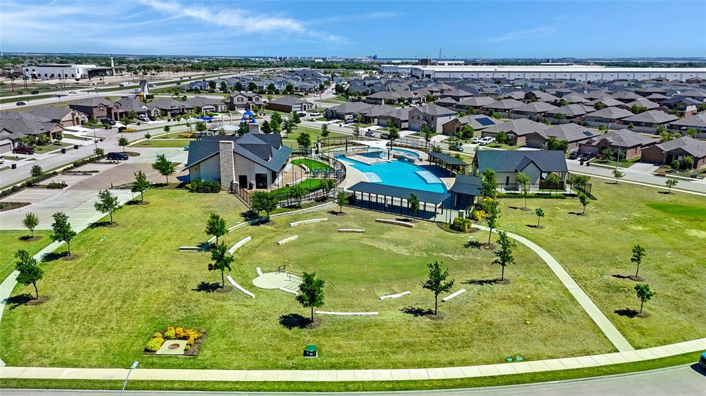1112 Croxley Way Justin, TX 76247 - Photo 16 of 18 Expansive community green space featuring a large lawn area with scattered trees, a winding paved pathway, and built-in seating elements