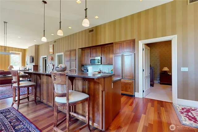 a kitchen with stainless steel appliances granite countertop a refrigerator a sink dishwasher a stove and a dining table with wooden floor