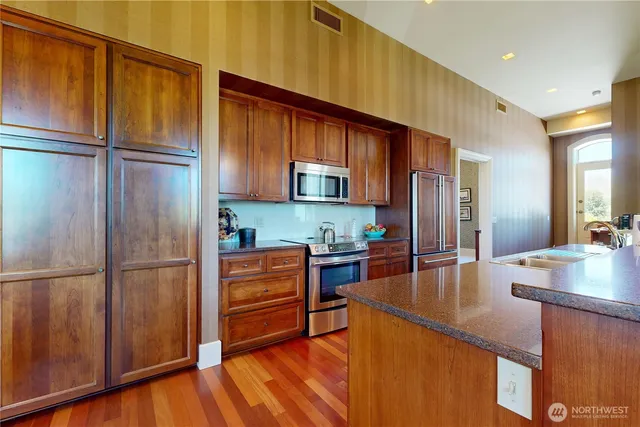 a kitchen with stainless steel appliances granite countertop a refrigerator a stove and a sink with wooden cabinets