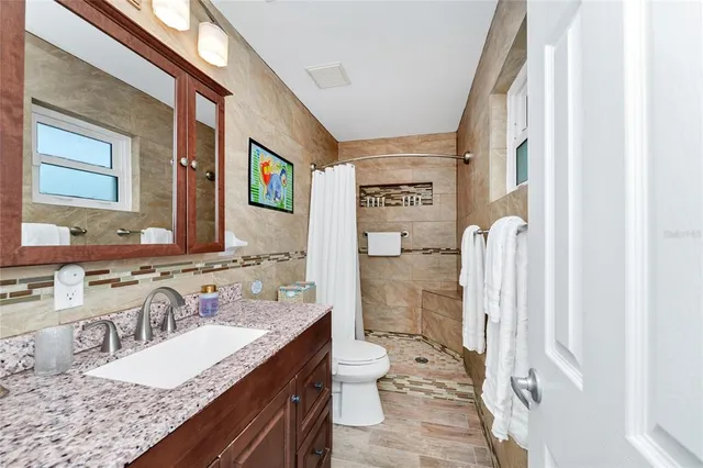a bathroom with a granite countertop sink a toilet a mirror and shower