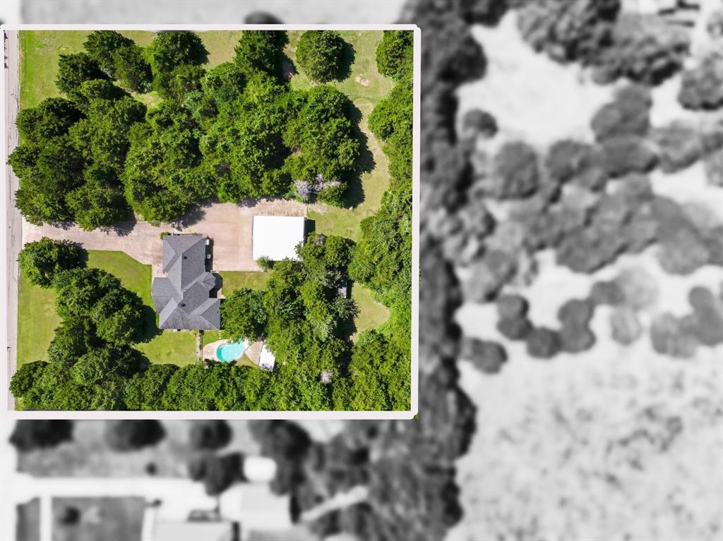 Aerial property overview featuring a dark-tiled roof, mature perimeter trees, a private swimming pool, a concrete driveway, and a detached white-roof structure