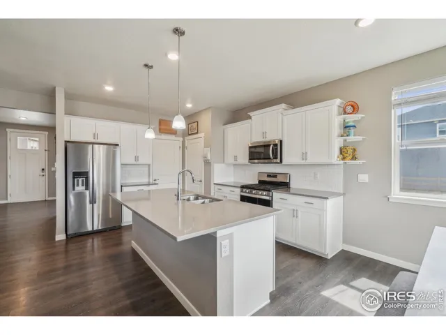 a kitchen with stainless steel appliances kitchen island a sink dishwasher a refrigerator a oven with white cabinets and wooden floor