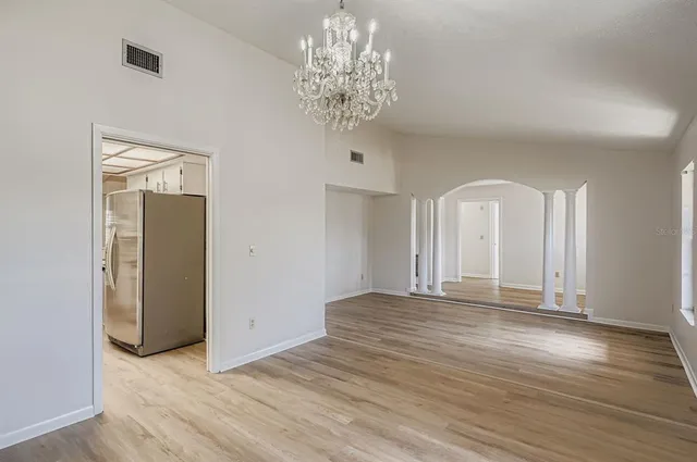 an empty room with wooden floor chandelier and windows
