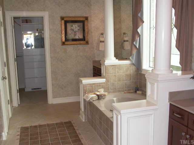 3915 Morvan Way Raleigh, NC 27612 - Photo 10 of 12 First floor master bath with separate vanity sinks and walk in California closet at the back. The whirlpool tub is trimmed with custom columns and the art glass window allows beautiful sunlight into the room. Separate shower includes bench seat.