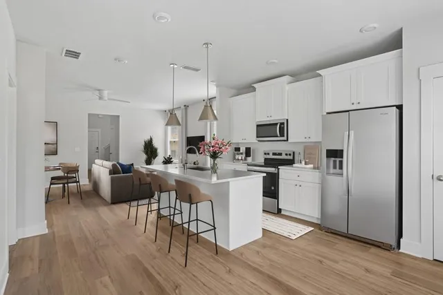 a kitchen with stainless steel appliances granite countertop a refrigerator a microwave oven a stove a dining table and chairs with wooden floor