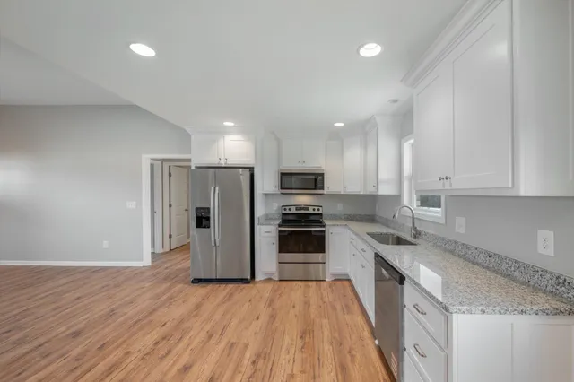 a kitchen with stainless steel appliances granite countertop a refrigerator a stove top oven a sink and dishwasher with wooden floor