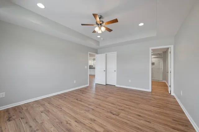 a view of an empty room with wooden floor and a ceiling fan