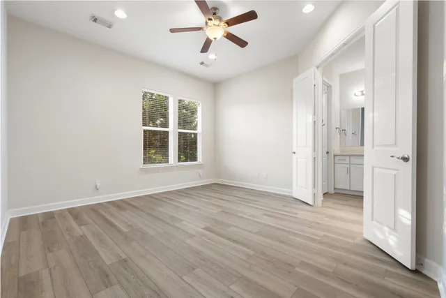 an empty room with wooden floor a ceiling fan and windows