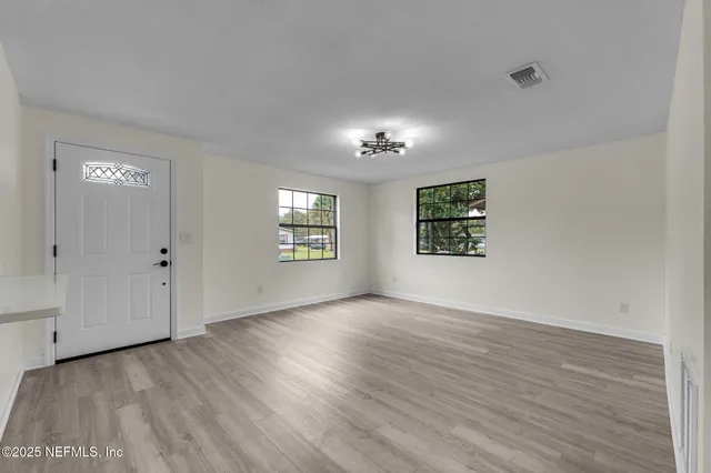 an empty room with wooden floor chandelier and windows