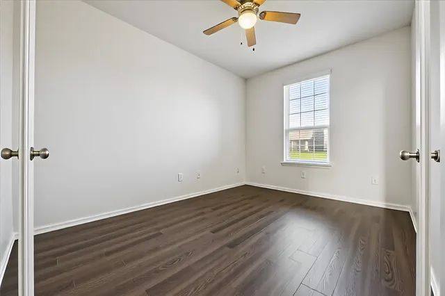 an empty room with wooden floor chandelier fan and windows