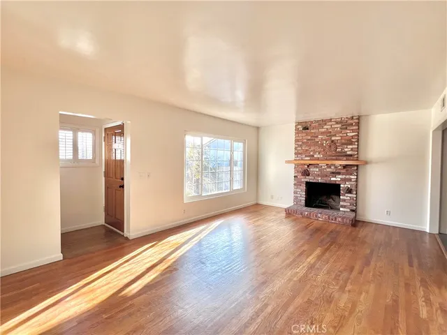 an empty room with wooden floor fireplace and windows