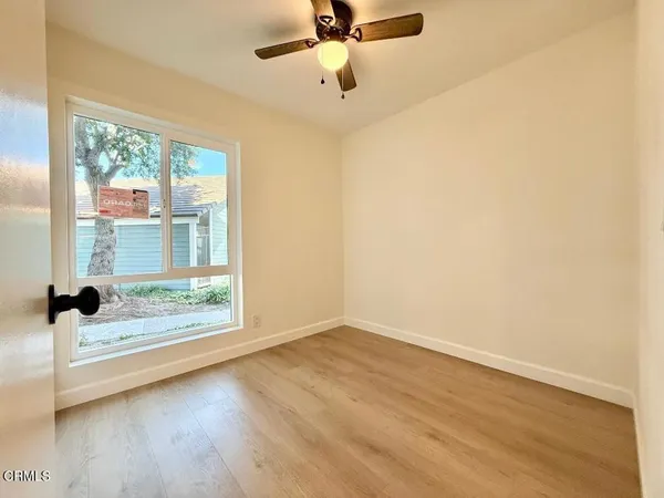an empty room with wooden floor fan and windows