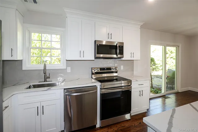 a kitchen with kitchen island granite countertop a sink cabinets stainless steel appliances and a window
