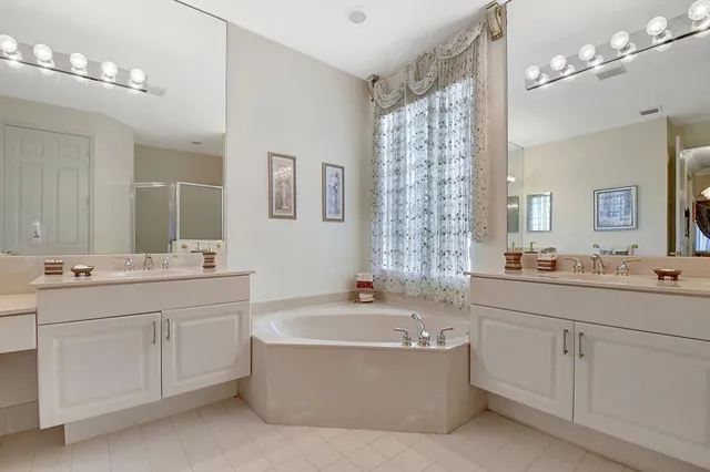 a bathroom with a bathtub a double vanity sink a vanity a lamp and a shower