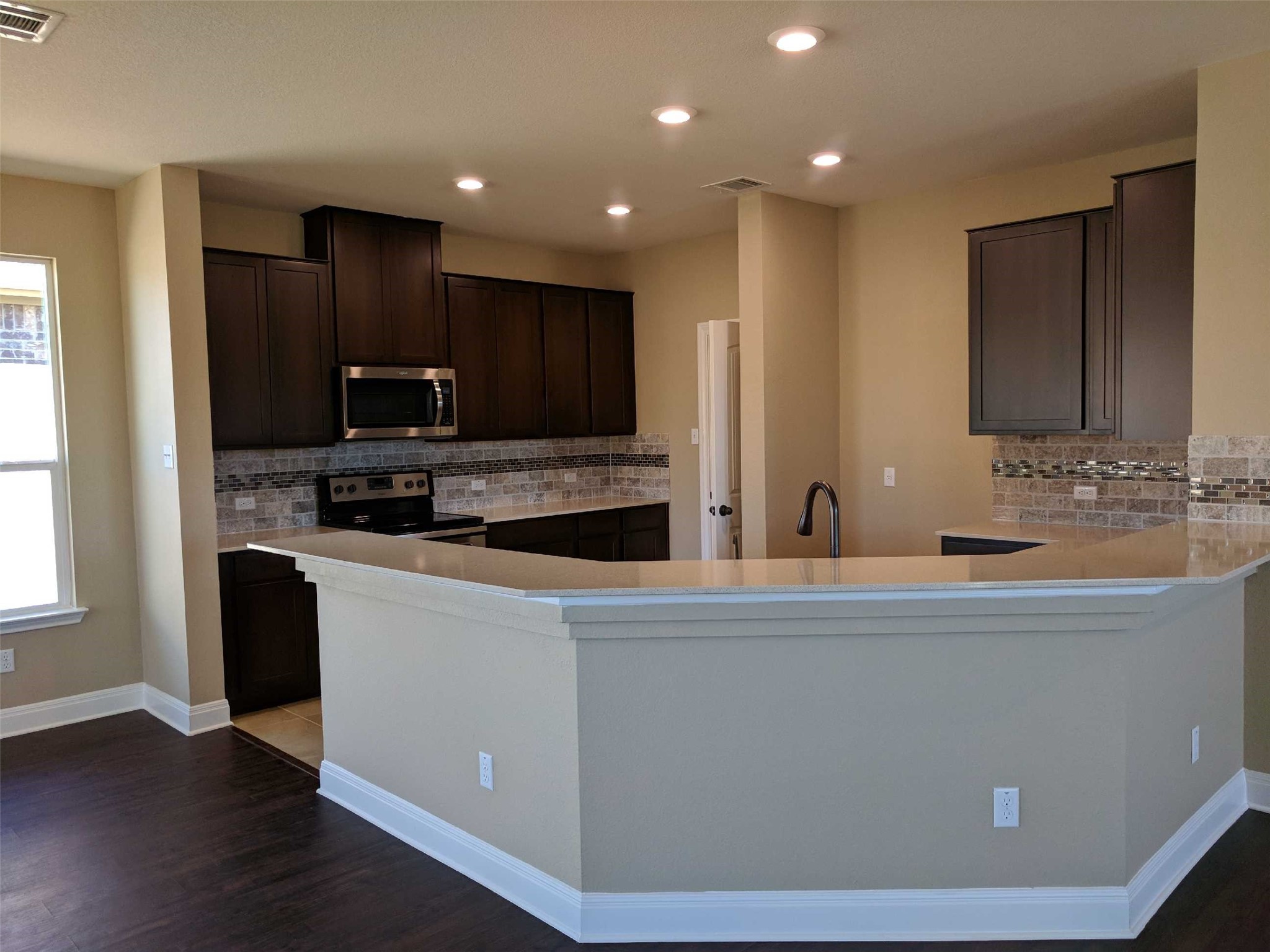 2471 Sunrise Road, Unit 8 Round Rock, TX 78664 - Photo 2 of 13 Open-concept kitchen featuring an expansive breakfast bar, dark wood-finish cabinetry, stainless steel appliances, and a mosaic tile backsplash