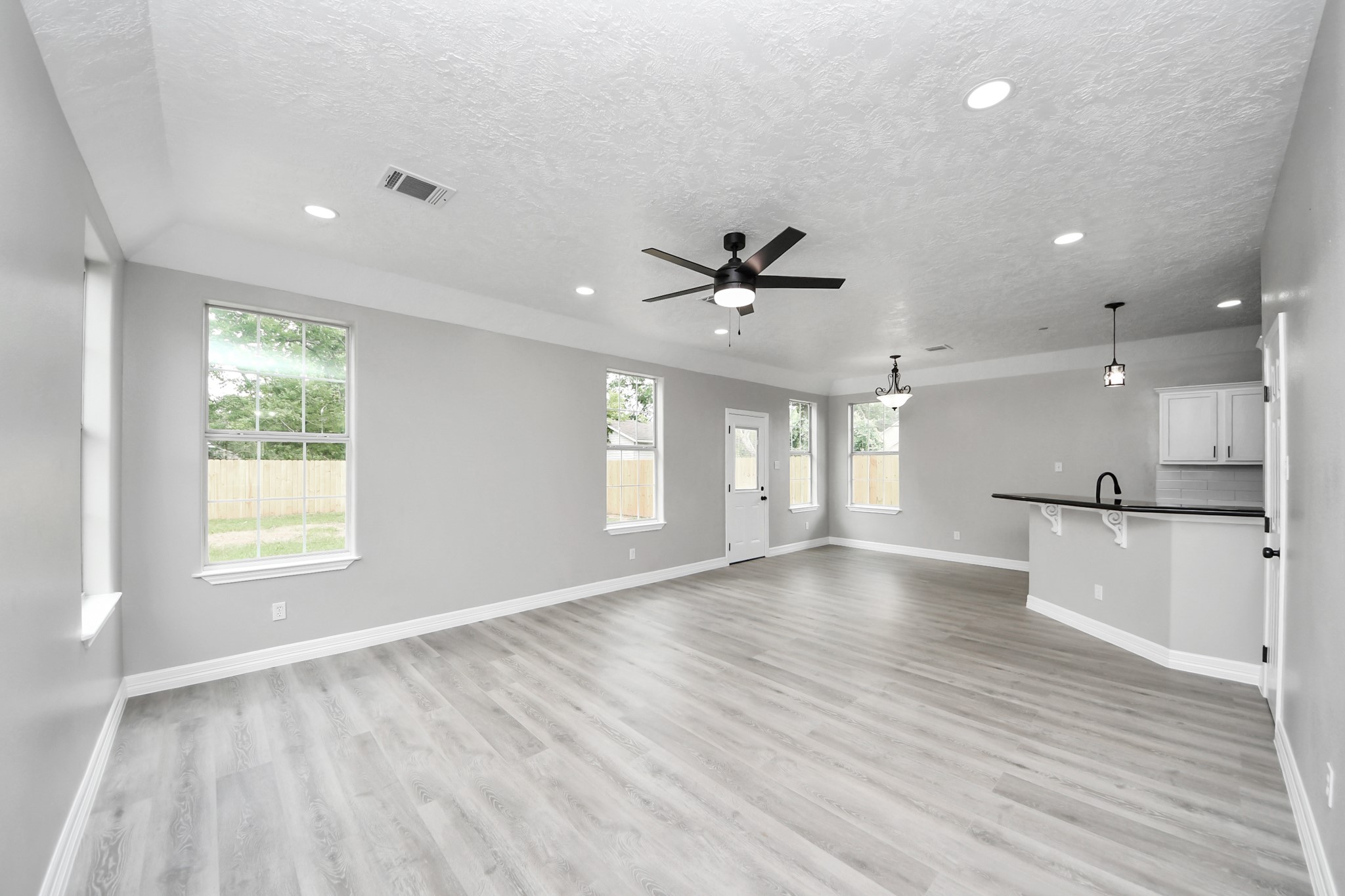 1105 East Kyle Road Clute, TX 77531 - Photo 3 of 44 A spacious, open-concept living area with modern gray flooring, neutral walls, and recessed lighting. Large windows provide plenty of natural light. The room seamlessly connects to the dining area and the kitchen with a high bar and contemporary fixtures.