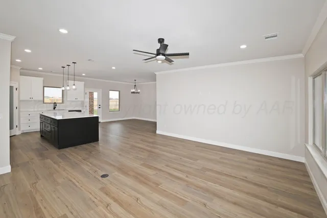 a living room with kitchen island a sink wooden floor and a ceiling fan