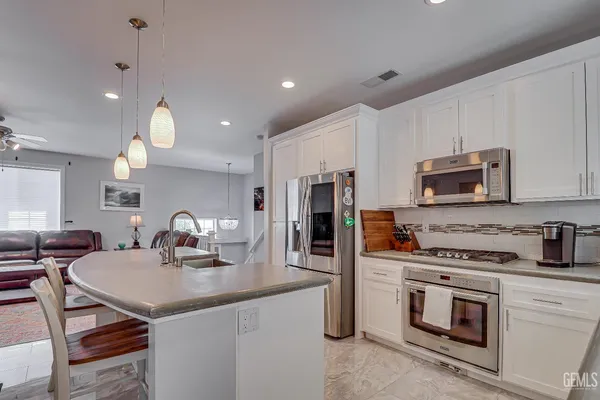 a kitchen with stainless steel appliances a stove a sink a microwave a refrigerator and white cabinets with wooden floor